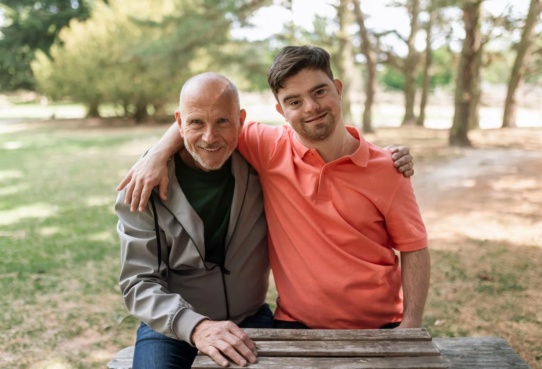 Happy senior father with his young son with Down syndrome embracing and sitting in park.